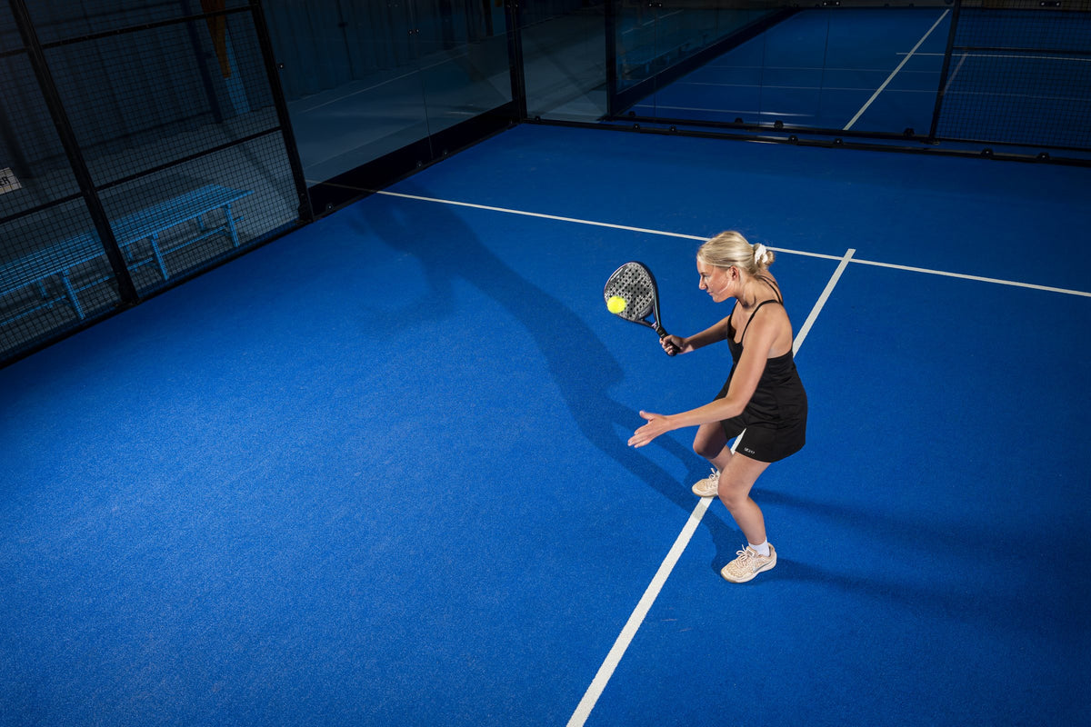 Padelspielerin im Ballwechsel auf dem blauen Court